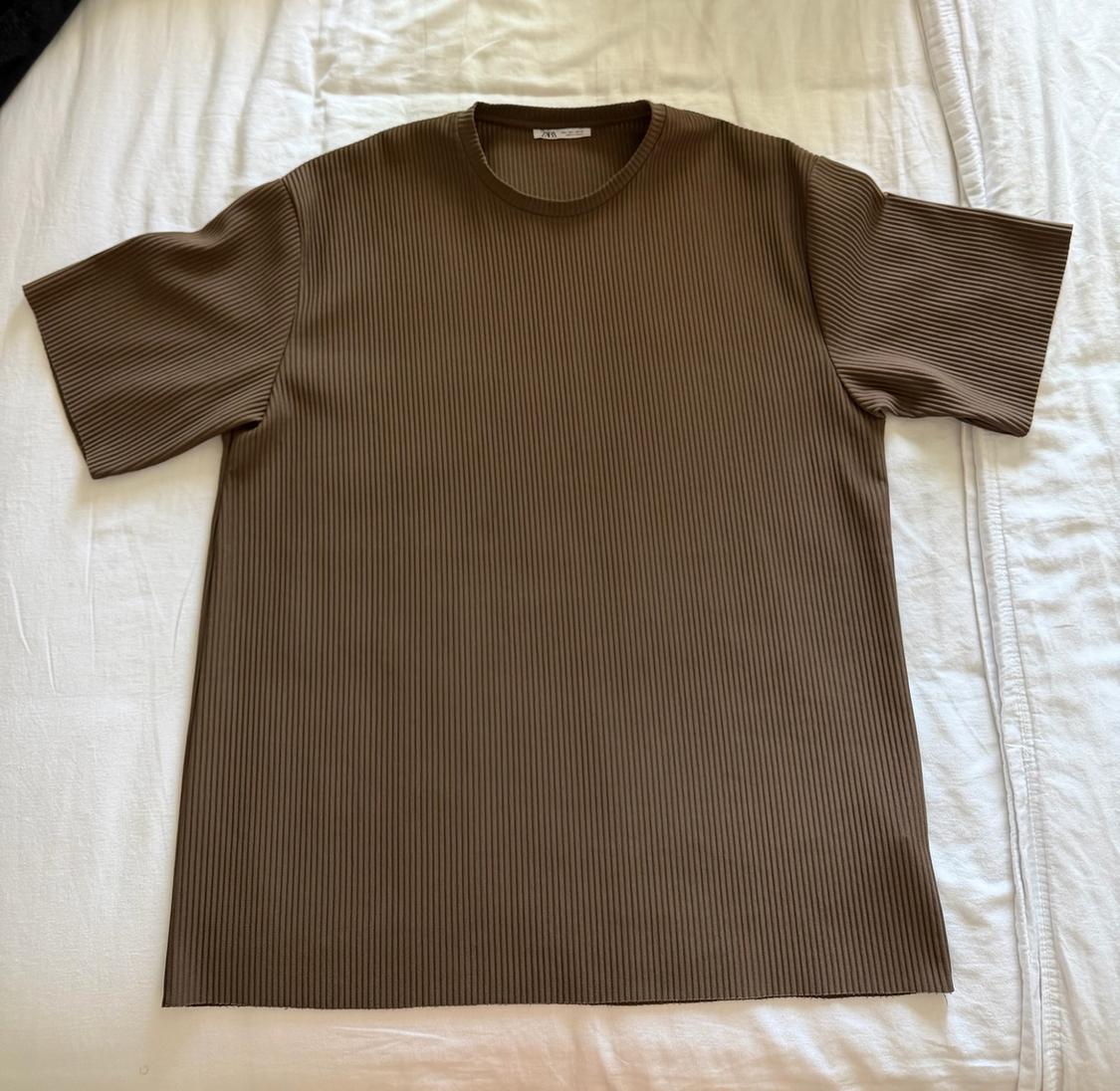 Brown short-sleeved ribbed T-shirt with ZARA label, laid out on a white sheet. Flat lay, casual style.