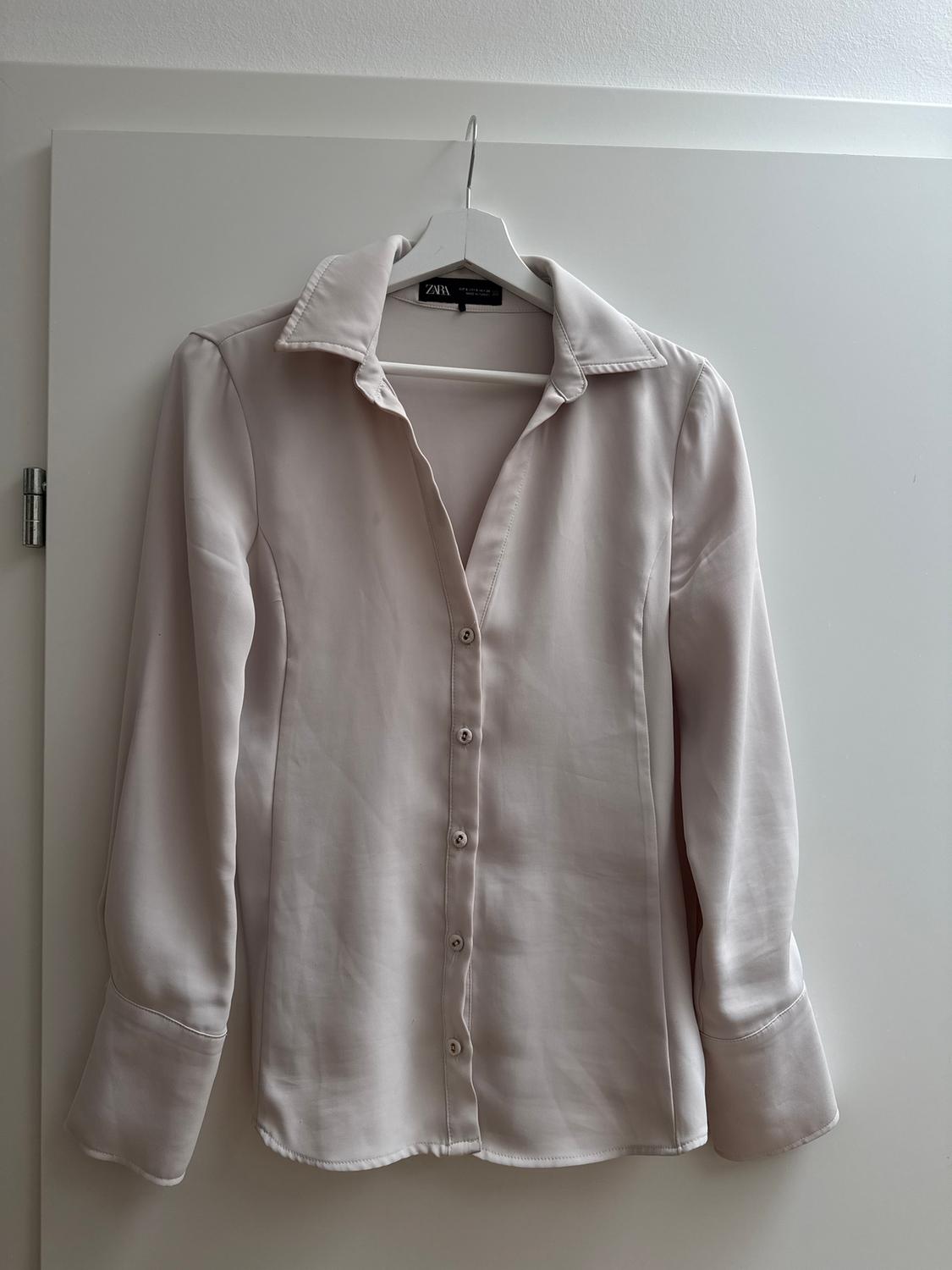 White long-sleeved shirt hanging on a white hanger over a door. Visible tag with the brand "Zara".