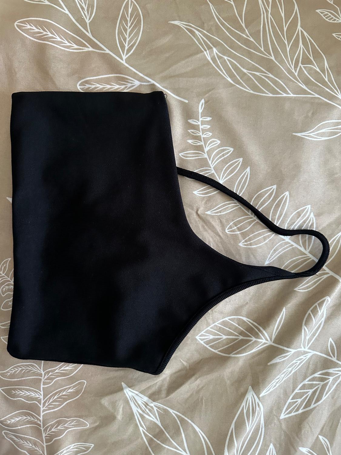 Black vest top with spaghetti straps over a beige fabric with a white leaf print.