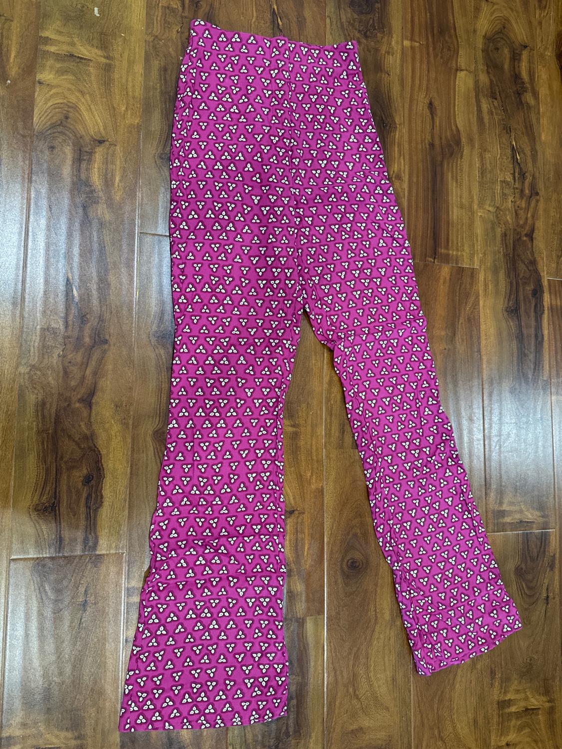 Pink flared trousers with a black and white triangle print, on a brown wooden floor.