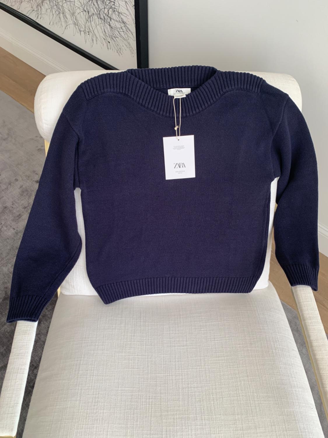 Navy jumper with a Zara label, placed on a white chair in a modern, minimalist setting.