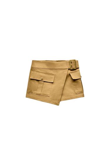 Beige mini skirt with large pockets and a buckle at the waist, on a white background.