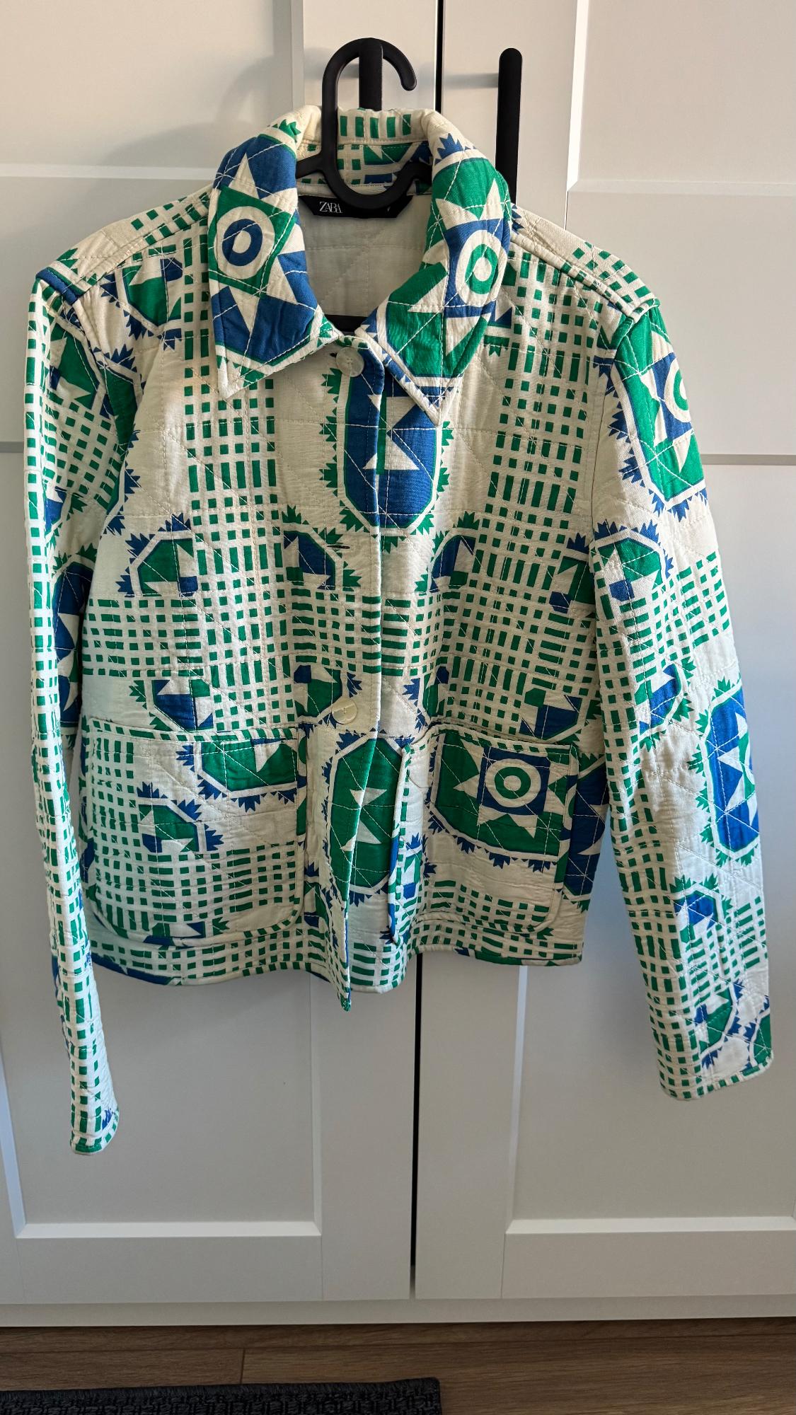 Jacket hanging with geometric print in green and blue on a white background, with front pockets and classic collar.