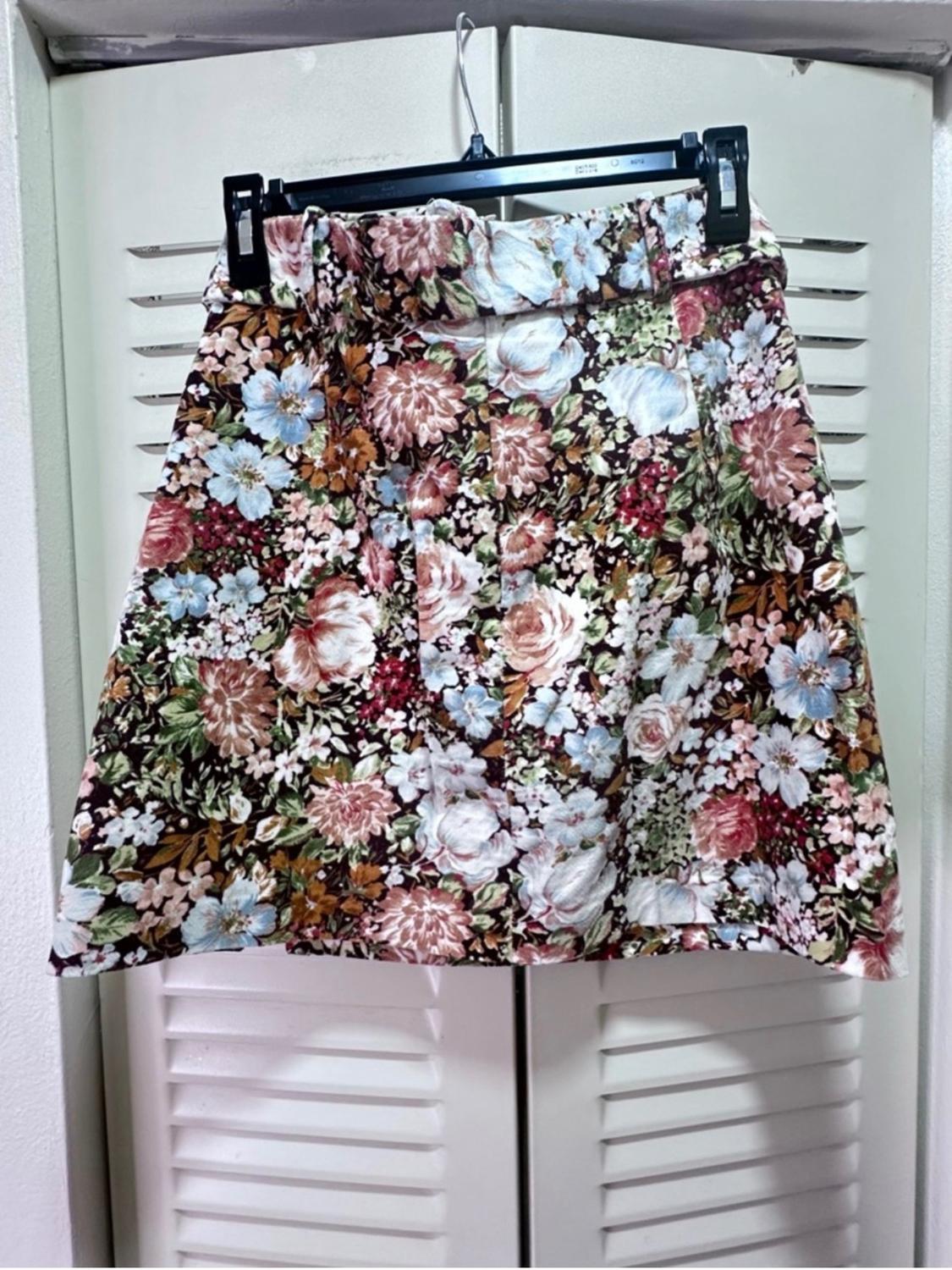Floral print hung skirt in shades of brown, pink, and blue, on a white background, in front of a white roller shutter door.