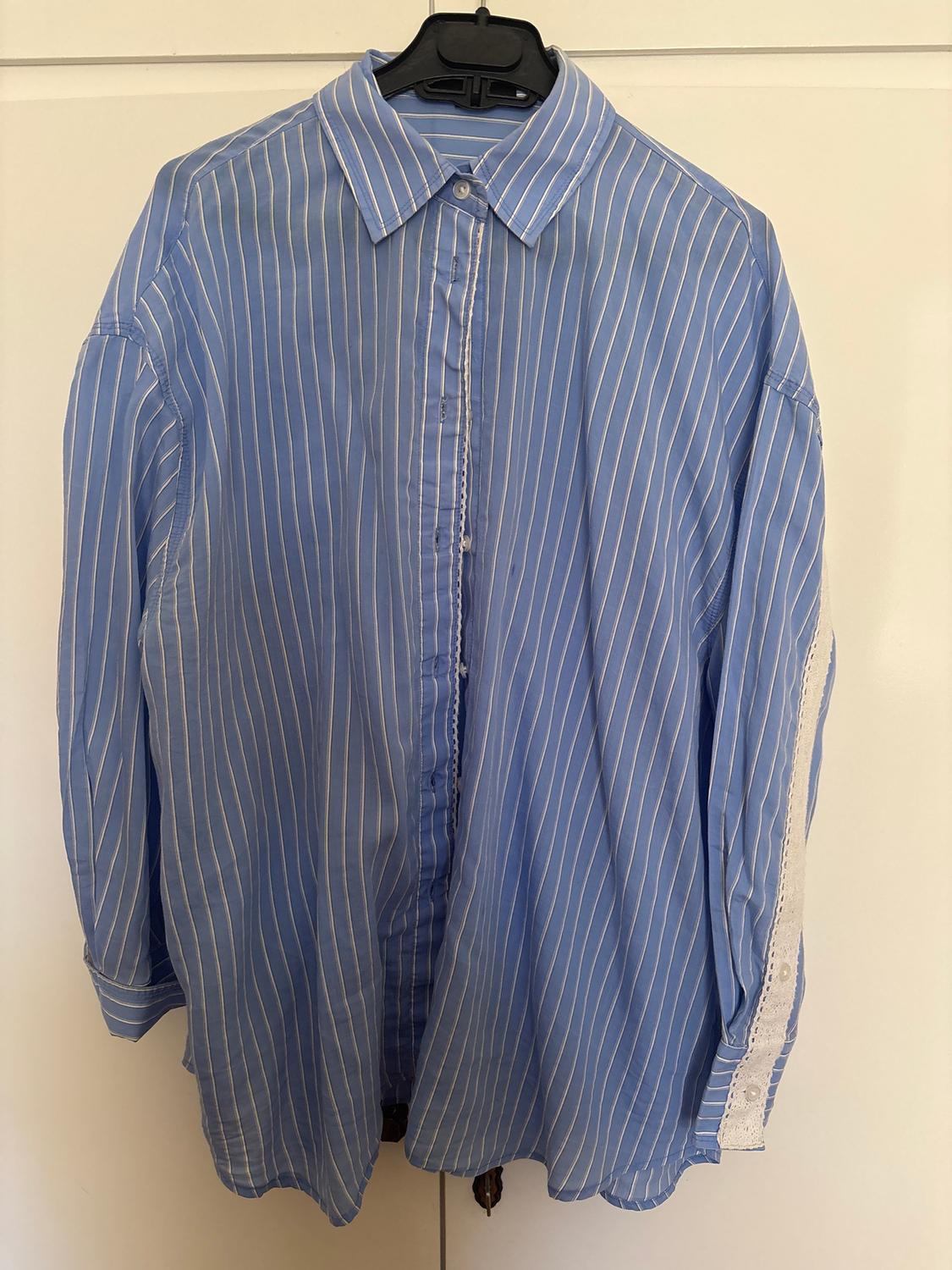 Blue shirt with white stripes hanging on a black hanger. White lace detail on the right sleeve. White background.