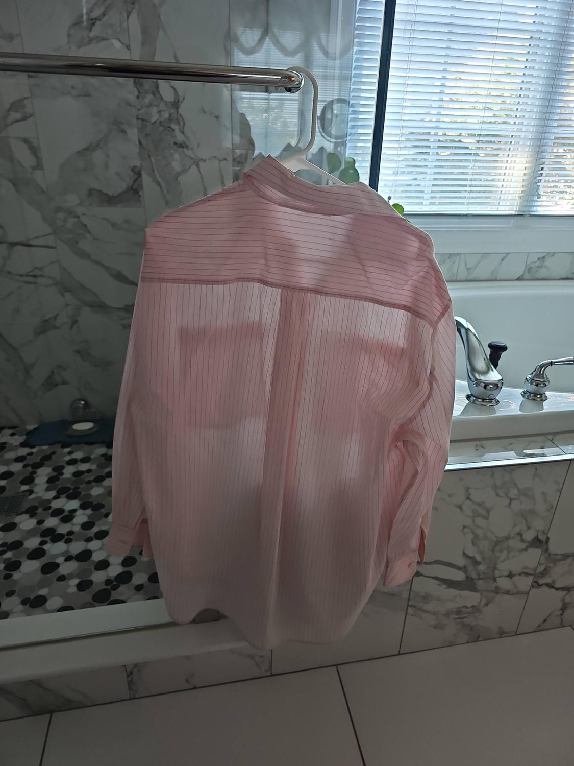 Light pink fine-striped shirt hanging on a hanger in a bathroom with marble tile and a bathtub.