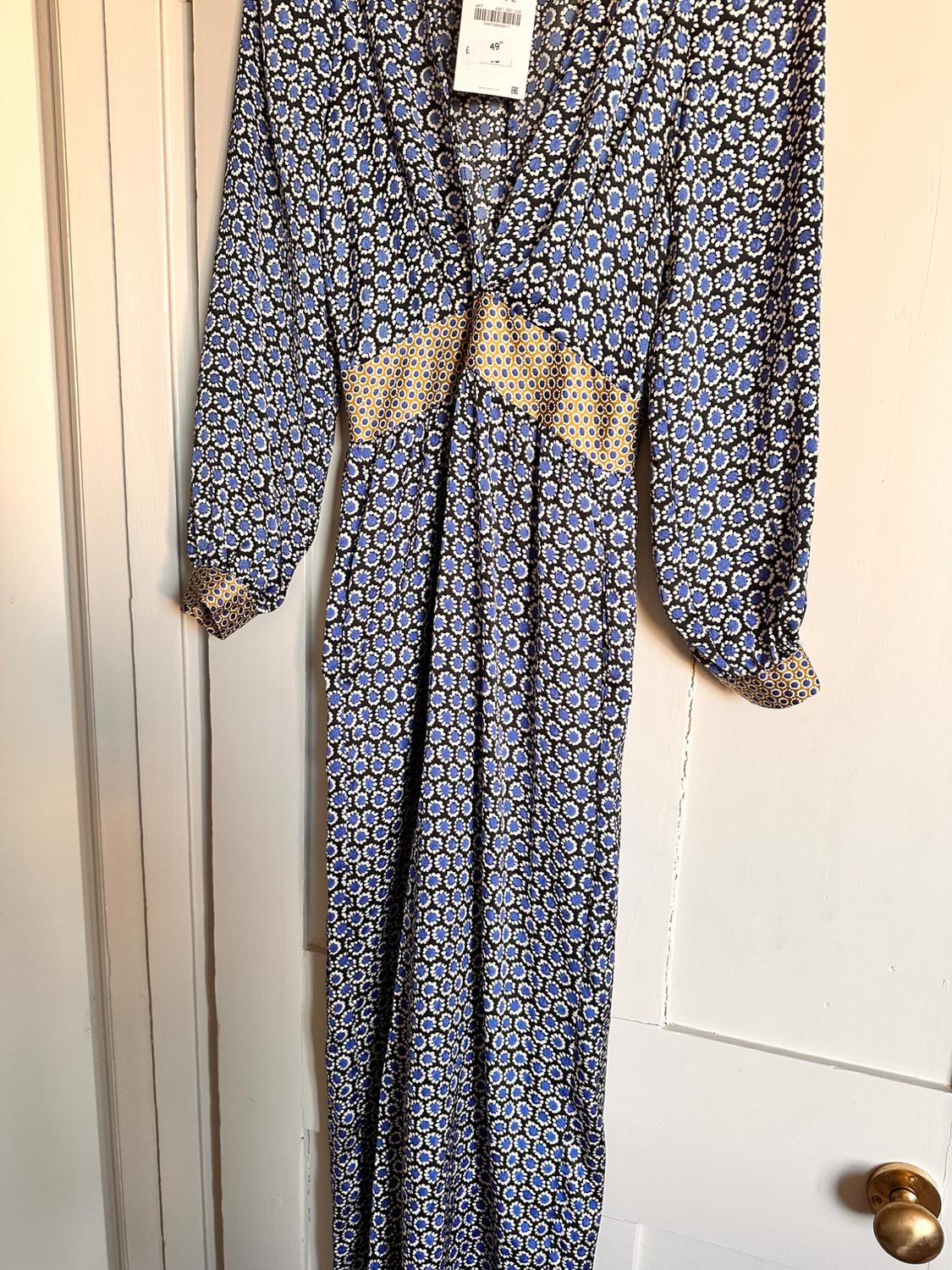 Long dress with blue and white geometric print, yellow detail at the waist, hanging on a white door. Price tag visible.