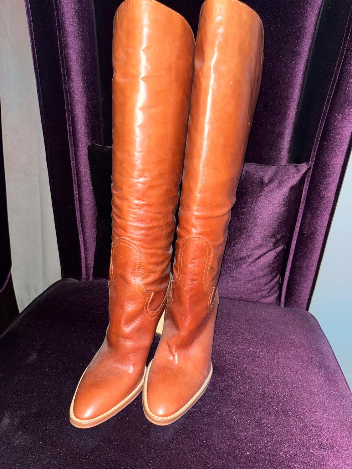 Brown leather knee-high boots on a purple velvet chair. The light highlights the sheen of the material.