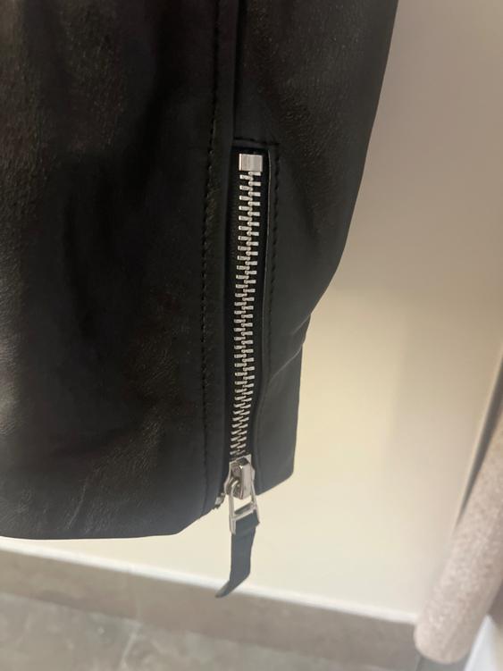 Detail of a black jacket with a silver metallic zipper in a lit indoor setting.