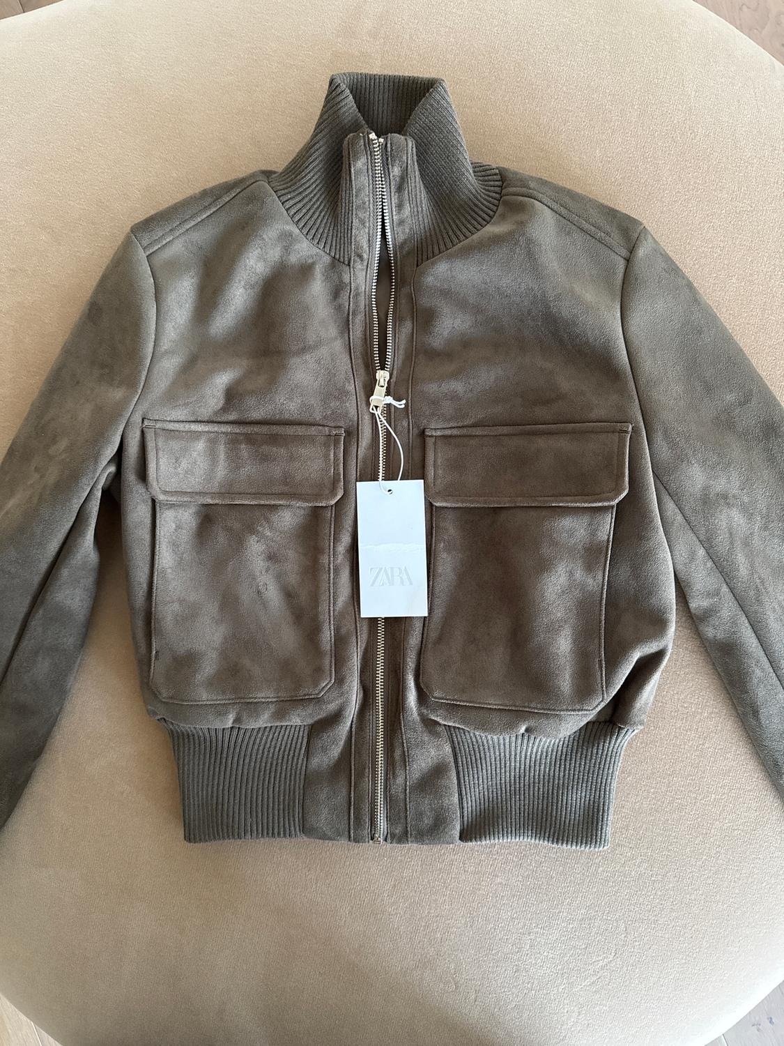 Brown zip-up jacket with a high collar on a beige background. Visible label with the text "ZARA".