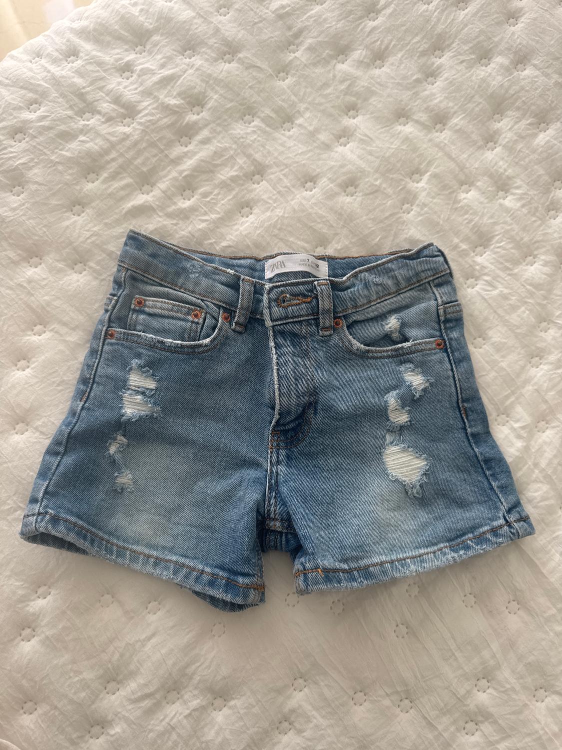 Distressed blue denim shorts on a white quilted bedspread. Label visible on waistband.