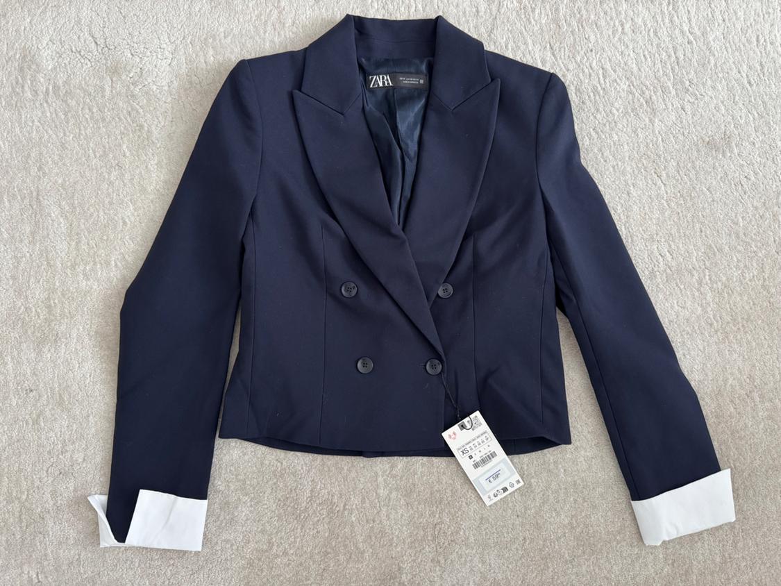 Navy blue double-breasted jacket with white lapels and cuffs, visible label with size and price details on a light background.