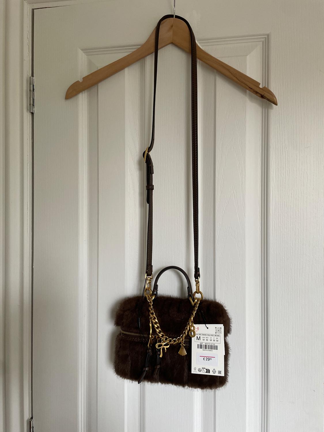 Brown handbag with a gold chain and a €29 price tag, hanging on a wooden hanger over a white door.