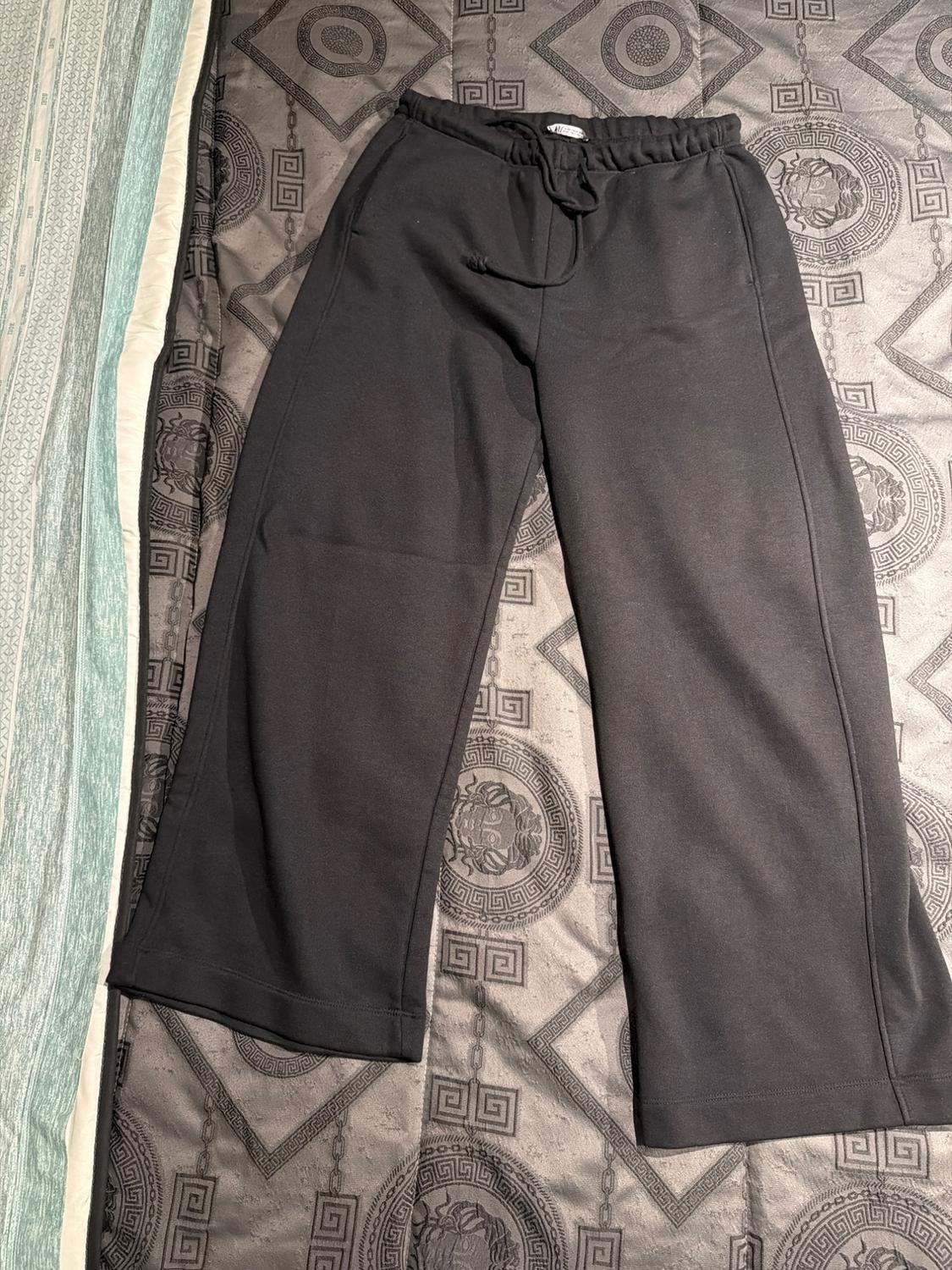 Black wide-leg trousers with an elasticated drawstring waist, on a grey duvet with geometric patterns and green detailing.