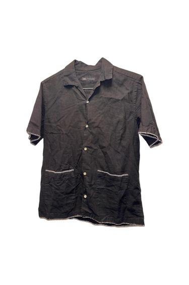 Black short-sleeved shirt with white buttons and two front pockets. White stitching details on the edges.