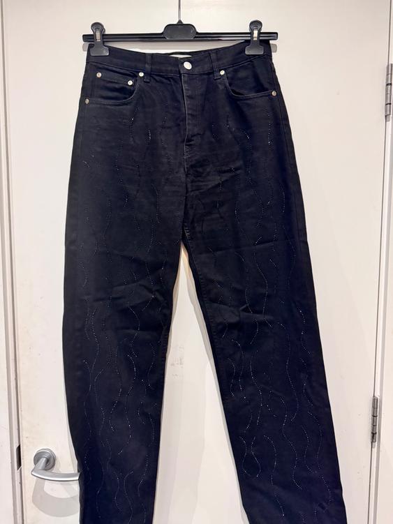 Black trousers hanging on a hanger, with a design of shiny wavy lines, over a white door with a silver handle.