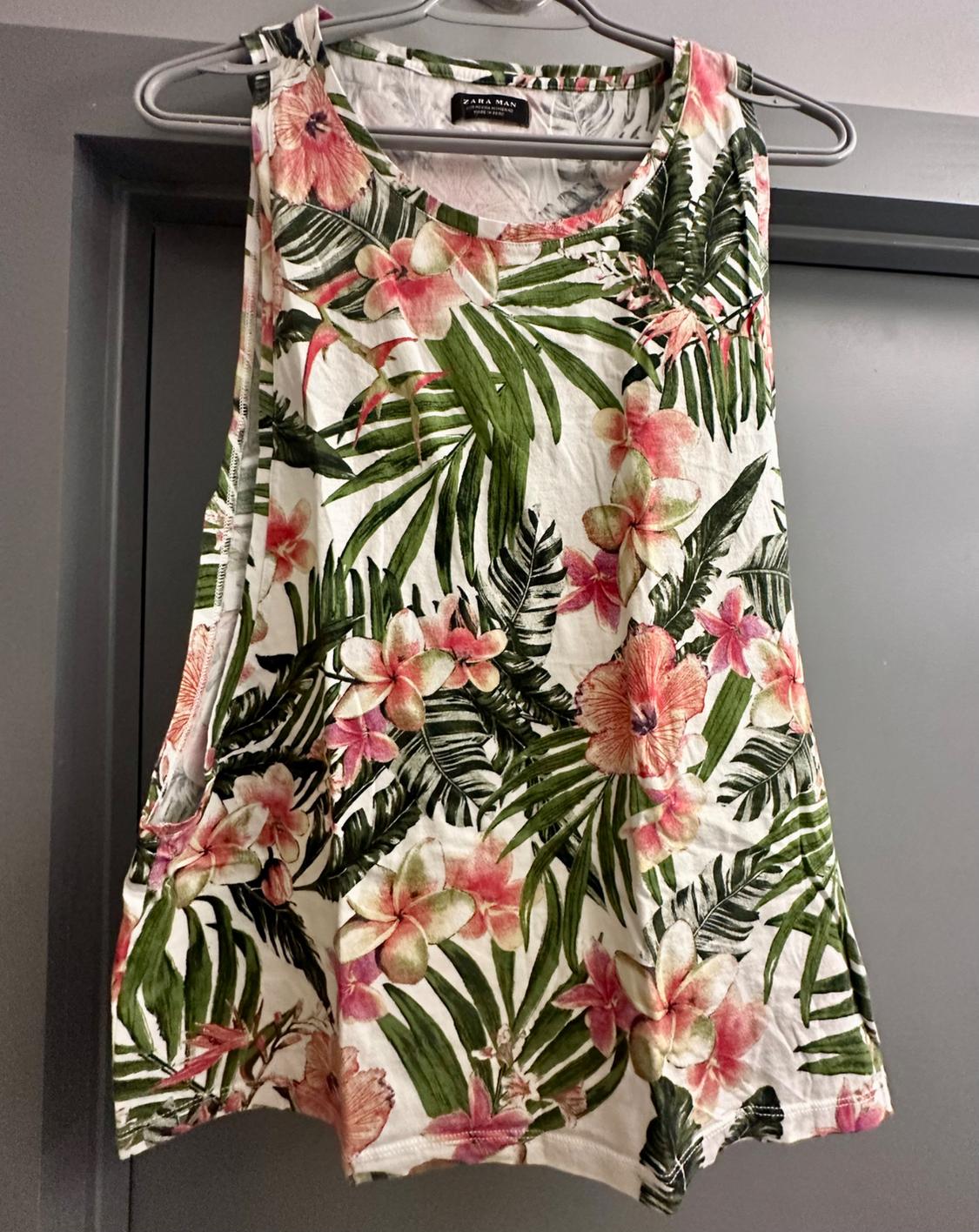 Front view of a sleeveless t-shirt with a tropical floral print in green and pink tones.