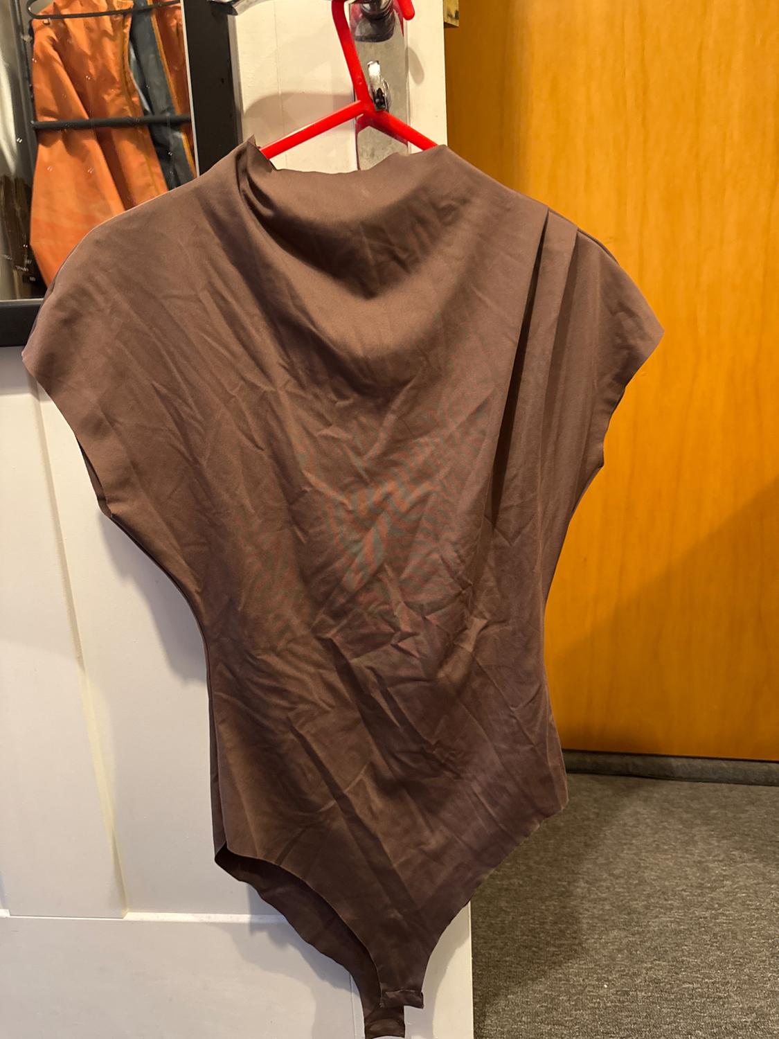 Brown bodysuit hanging on a red hanger above a white door. Reflection of clothes in a mirror in the background. Interior setting.