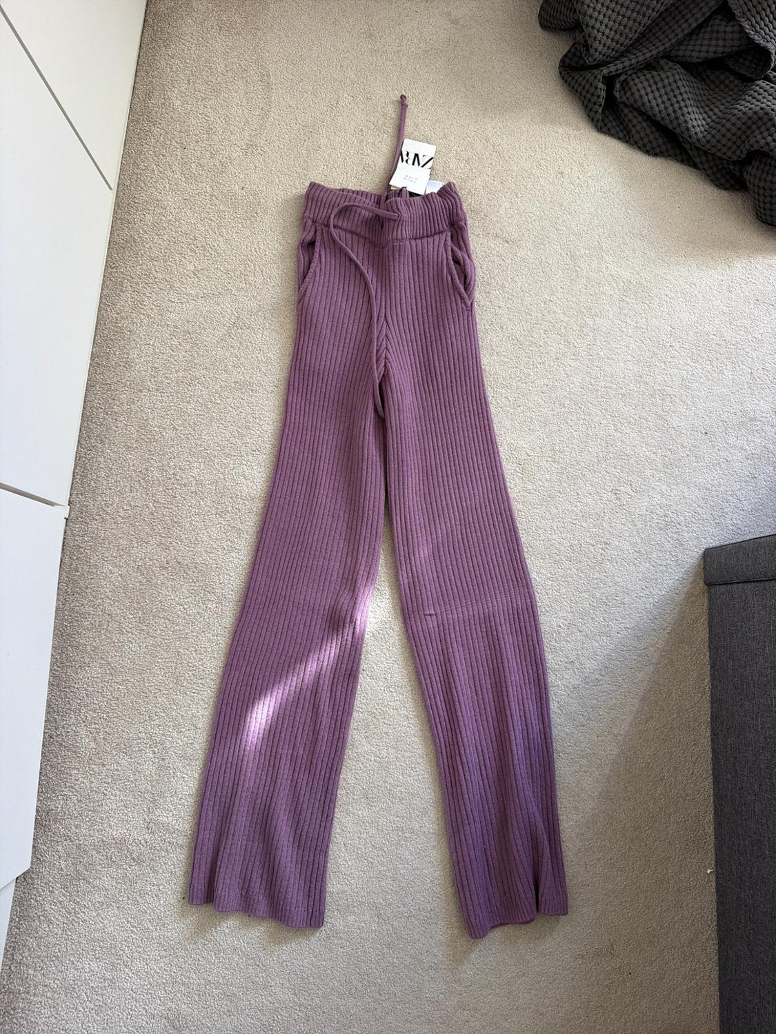 Purple ribbed knit trousers with a drawstring waist, on a light-coloured rug. Label with the text zara.