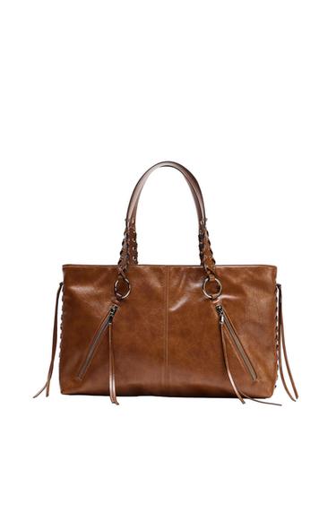 Brown handbag with plaited handles, two diagonal front zips with long pullers, and plaited details with fringing at the sides.