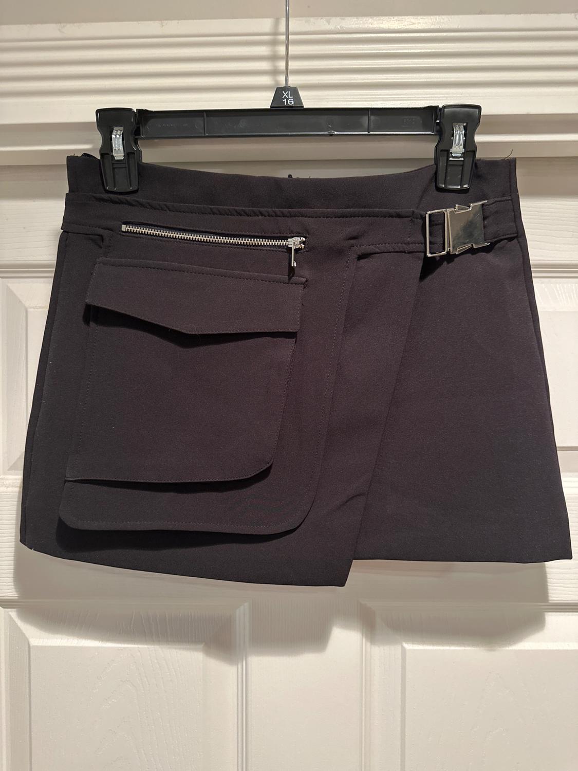 Black skirt with a large zip pocket, hung on a black hanger with an "XL 16" tag, on a white door.