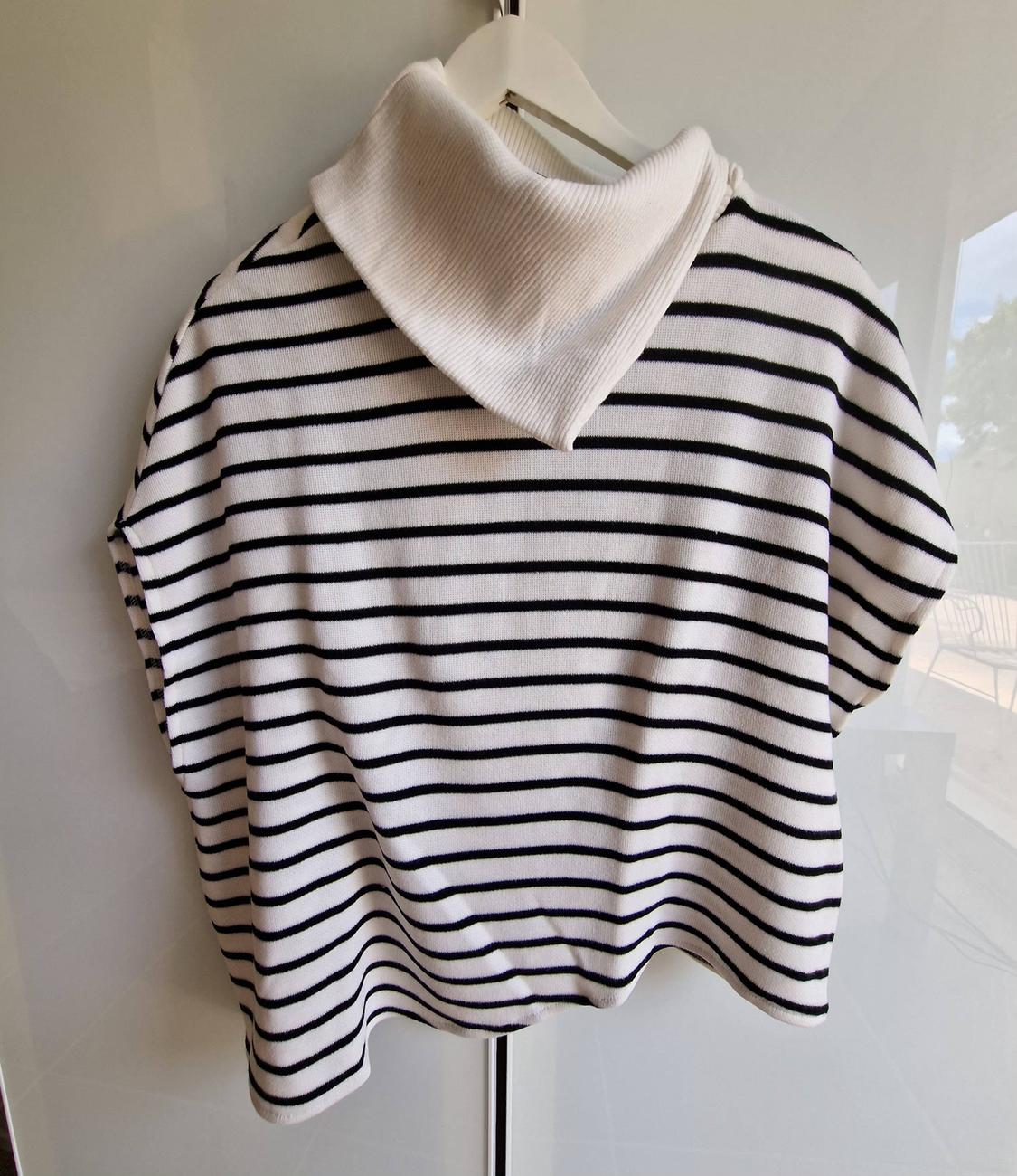 White knitted jumper with black stripes and a roll neck, hanging on a hanger against a white background.
