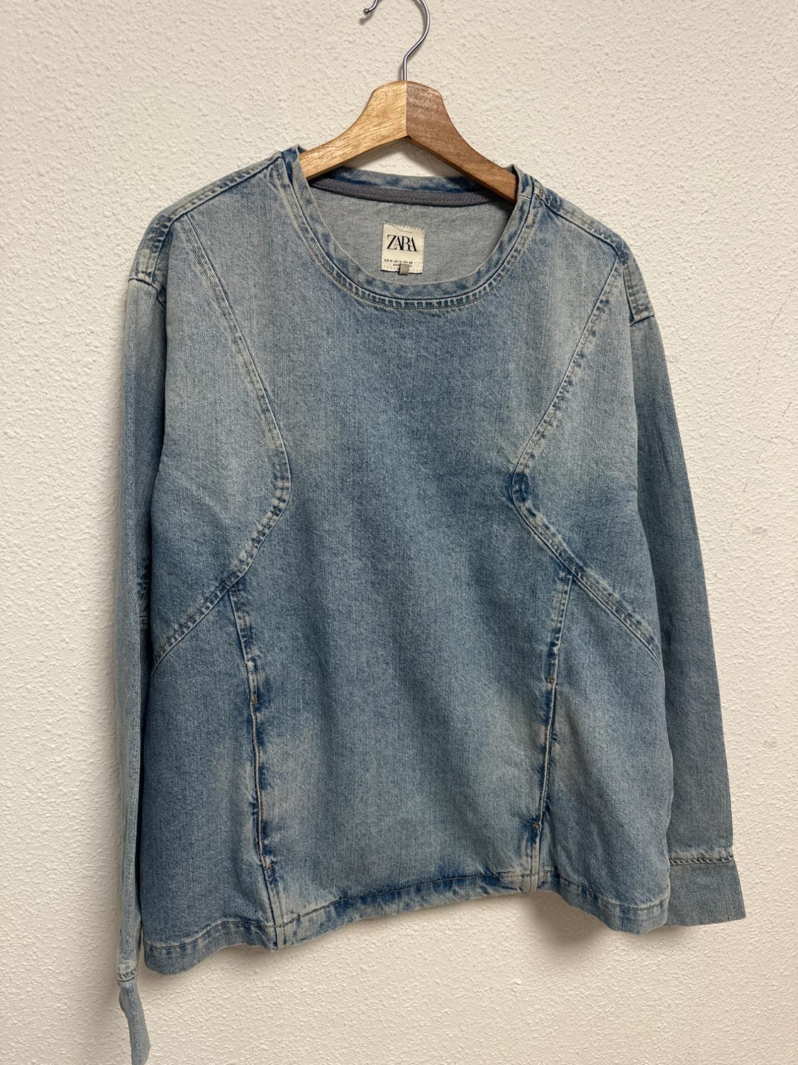 Light blue denim shirt hanging on a wooden hanger, with a visible label that says "ZARA", against a white wall.
