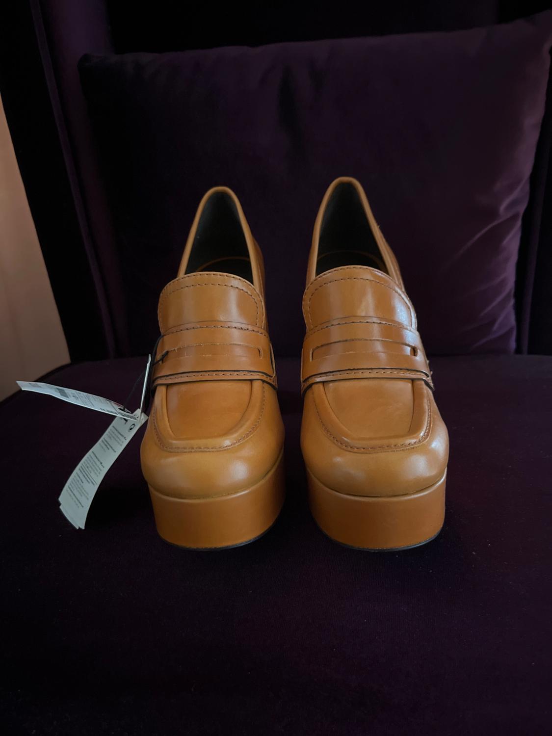Light brown platform shoes on a dark background, with visible hanging tags on the left side.