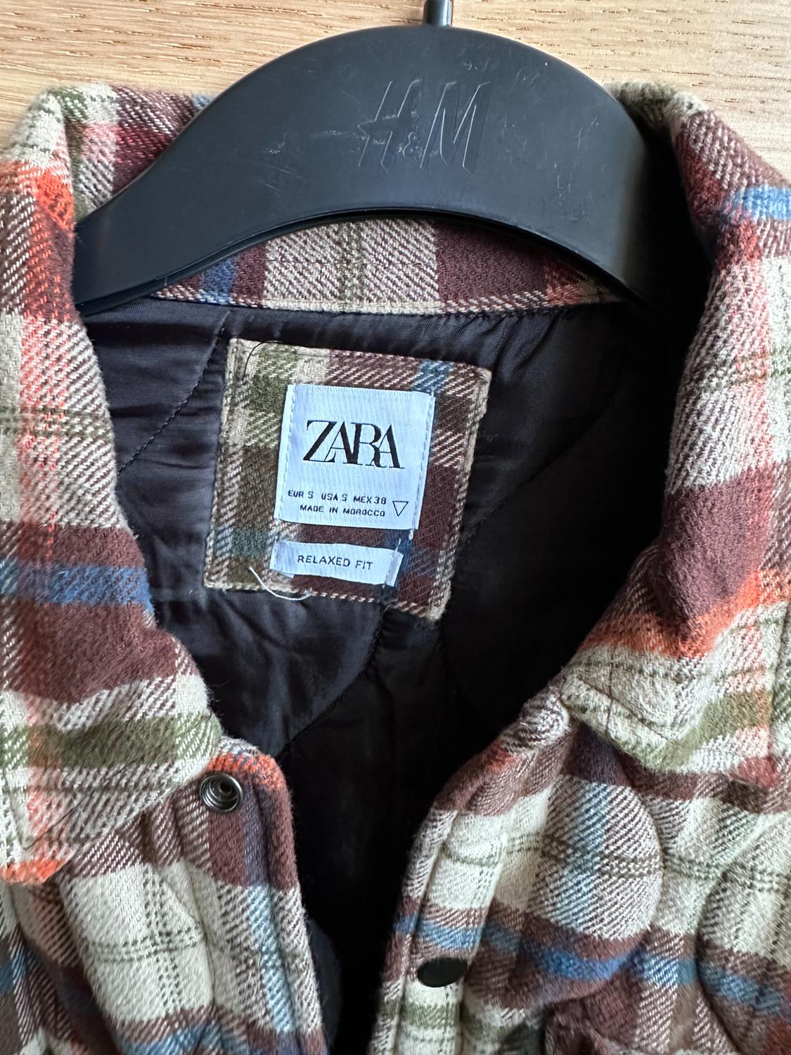Brown, green, and blue checked shirt on a black hanger with "H&M" logo. Inside label: "ZARA, RELAXED FIT, MADE IN MOROCCO".