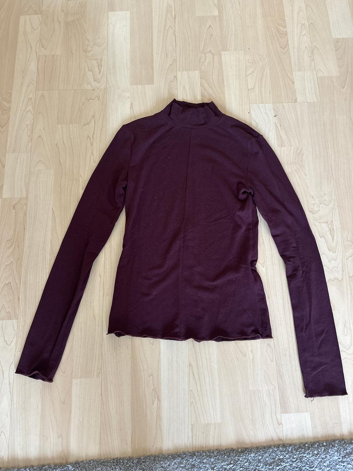 Burgundy long-sleeved roll neck jumper, spread out on a light wooden floor.