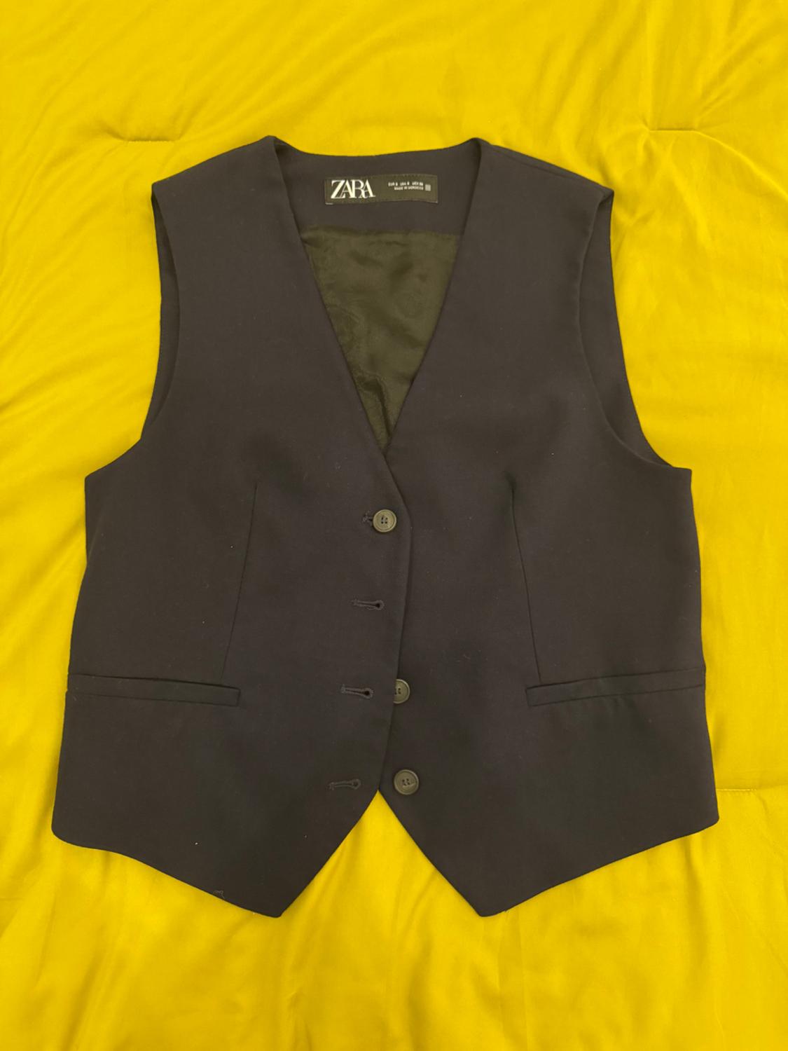 Black button-down vest on a yellow background. Visible label with text: "ZARA".