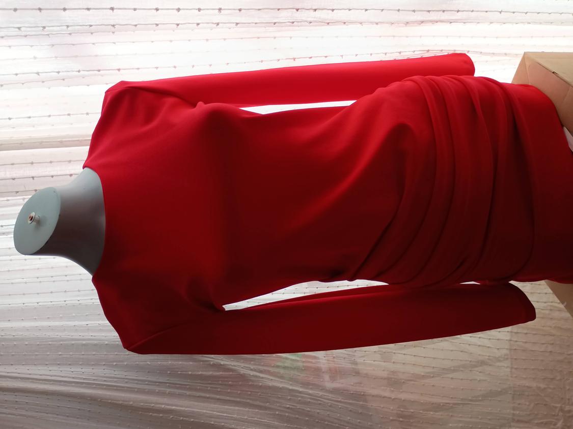 Tight red dress on a mannequin, with a translucent white curtain background. The design features pleats at the waist.