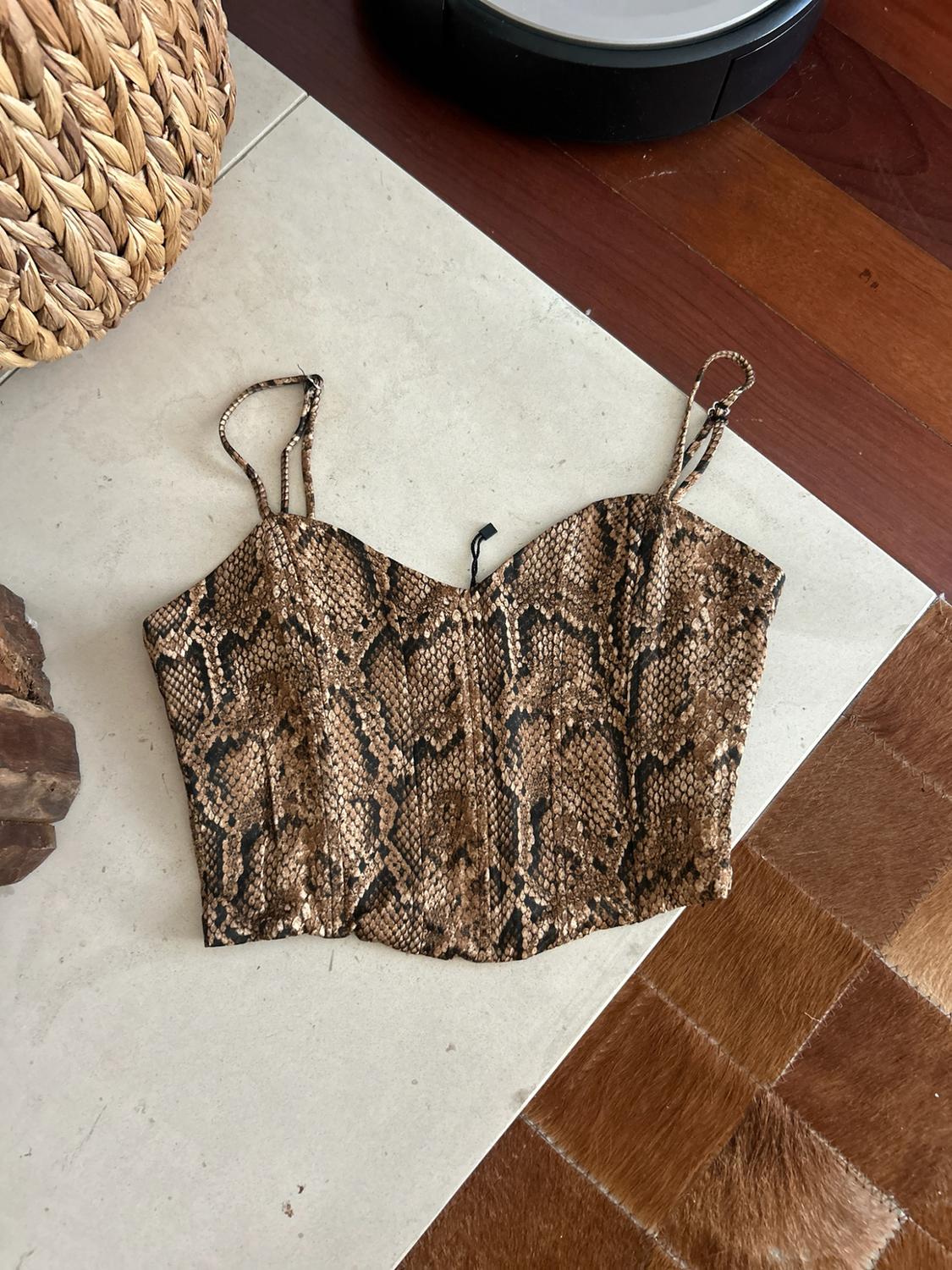 Cropped vest top with a brown and black snake print, laid on a light-coloured surface next to a wicker basket.