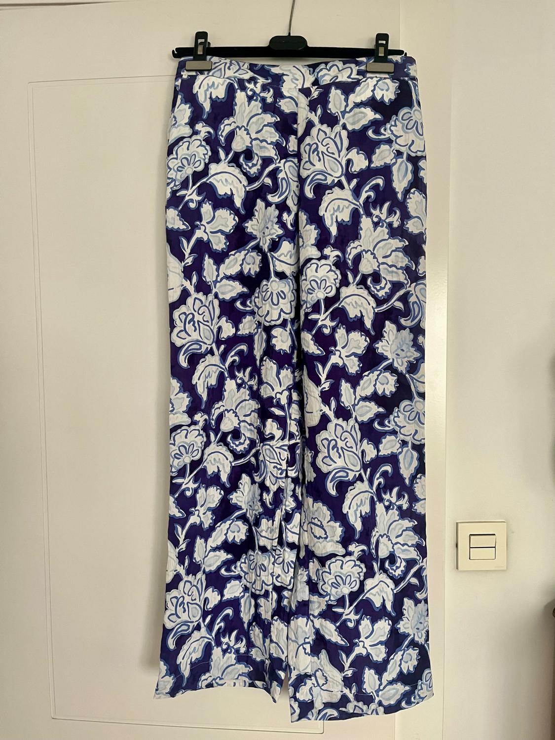 Trousers hanging with a blue and white floral print, light background. They're on a hanger over a white door.