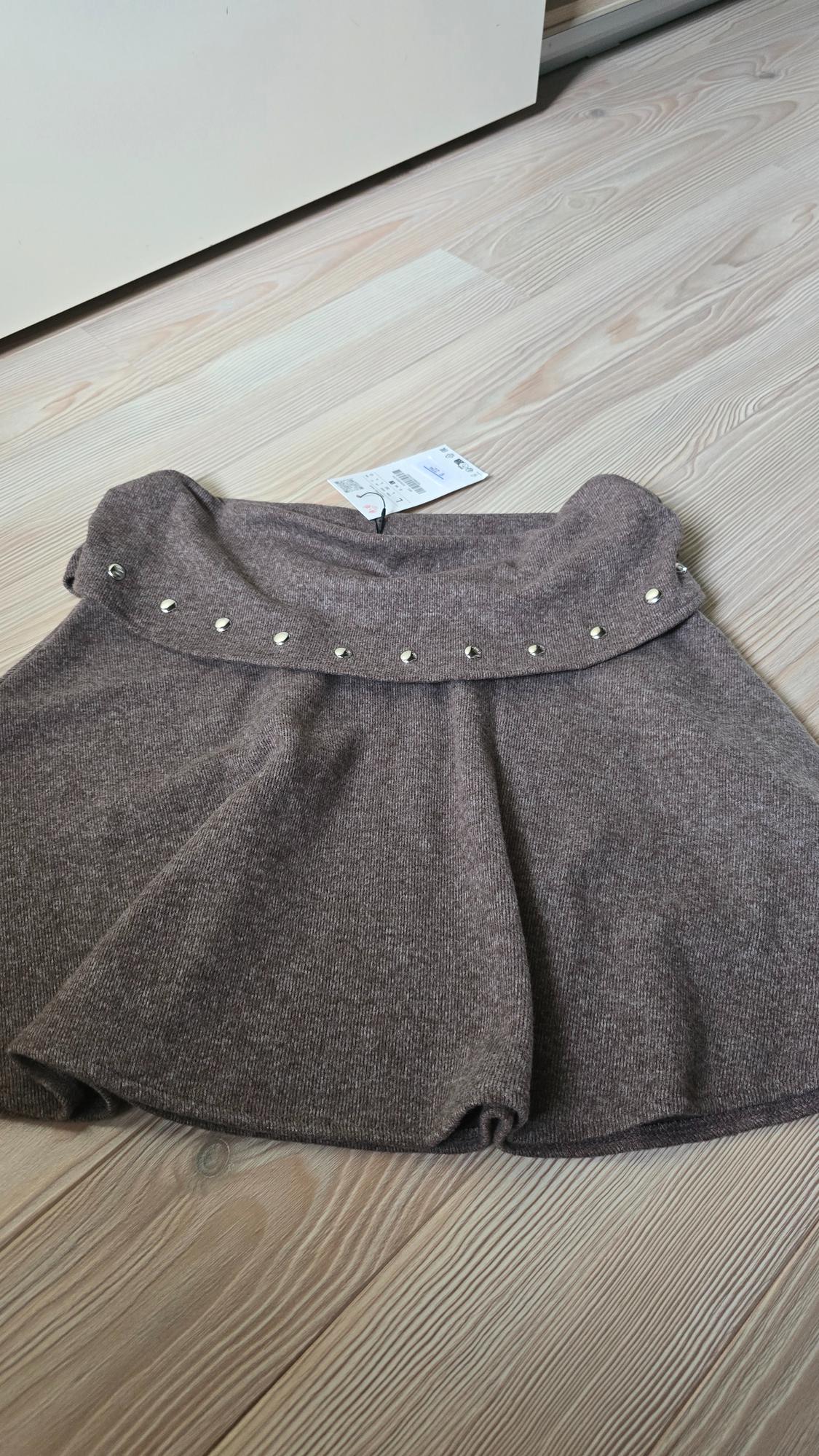 Brown skirt with silver studs on the waistband, on a light wooden floor. Visible label with barcode.