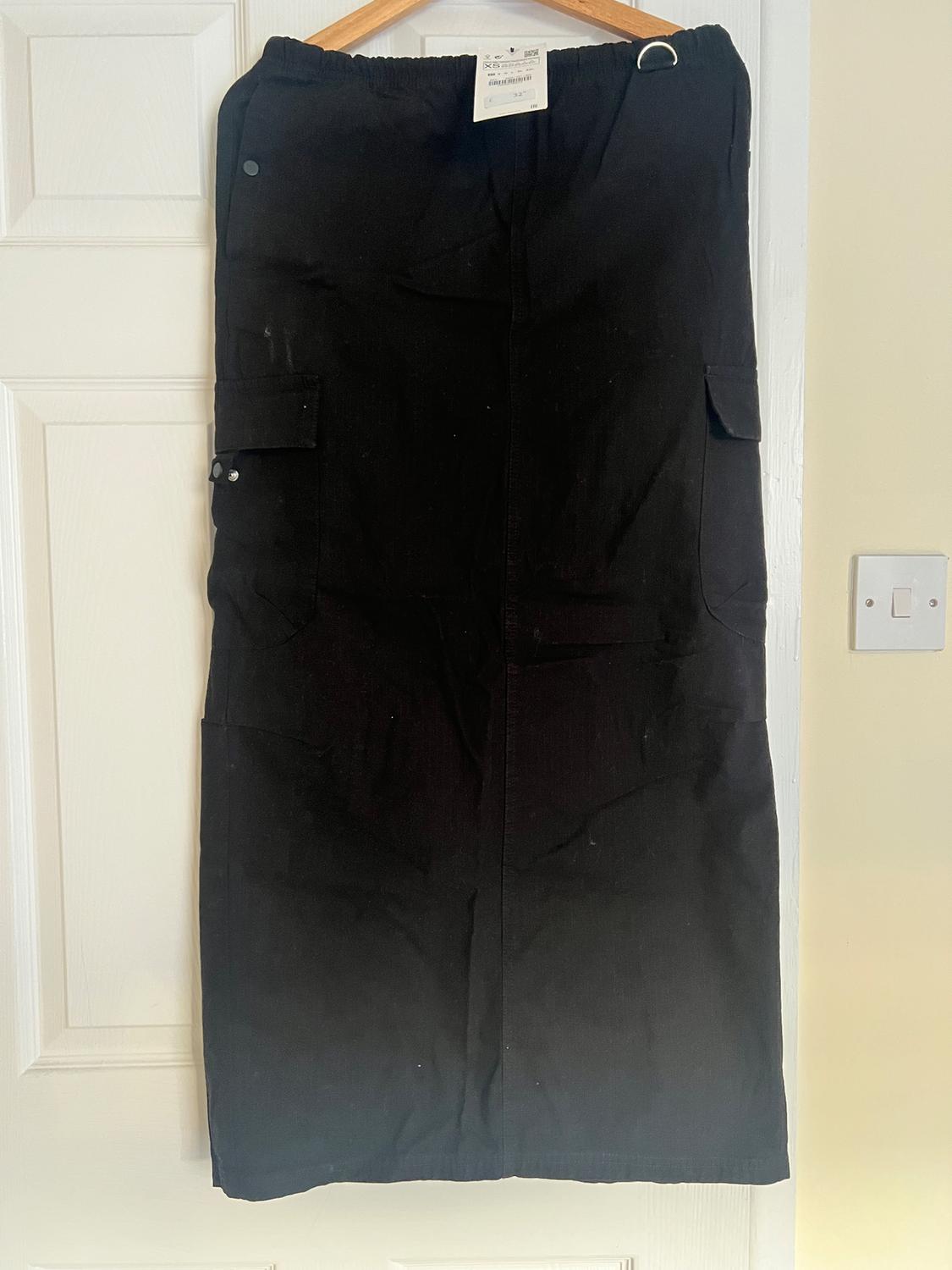 Black skirt hanging on a hanger over a white door. It has side pockets and a visible tag at the top.