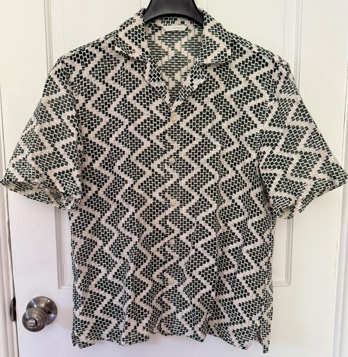 Short-sleeved shirt with a black and white geometric pattern, hanging on a hanger over a white door.