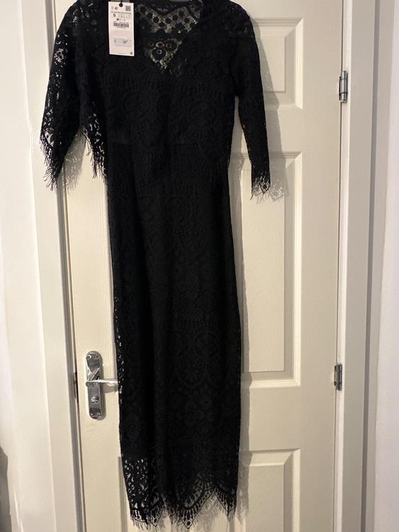 Black lace dress hanging on a white door, with visible tag on the left shoulder.