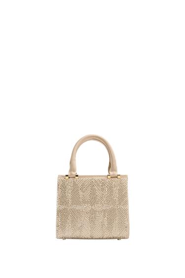Front view of a rigid beige purse with pearl embroidery, a handle, and a flap closure with a magnet.