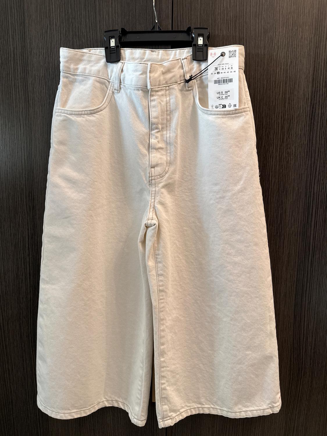 Beige shorts hanging on a black hanger with a visible tag. Dark wooden background.