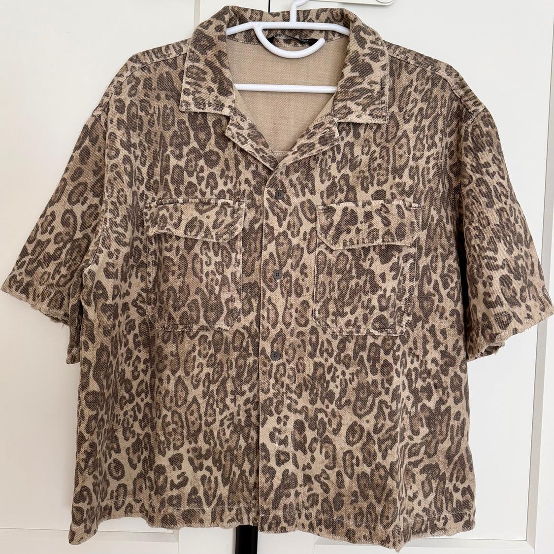 Short-sleeved leopard print shirt in brown tones, hanging on a white hanger against a light background.