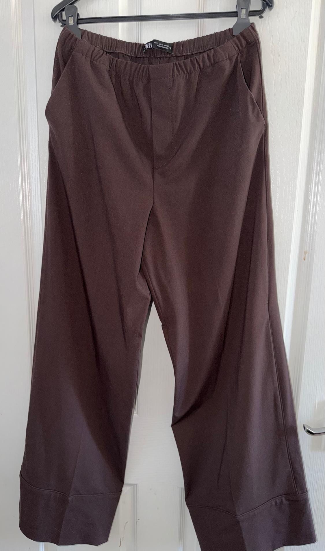 Brown wide-leg trousers hanging on a black hanger over a white door.