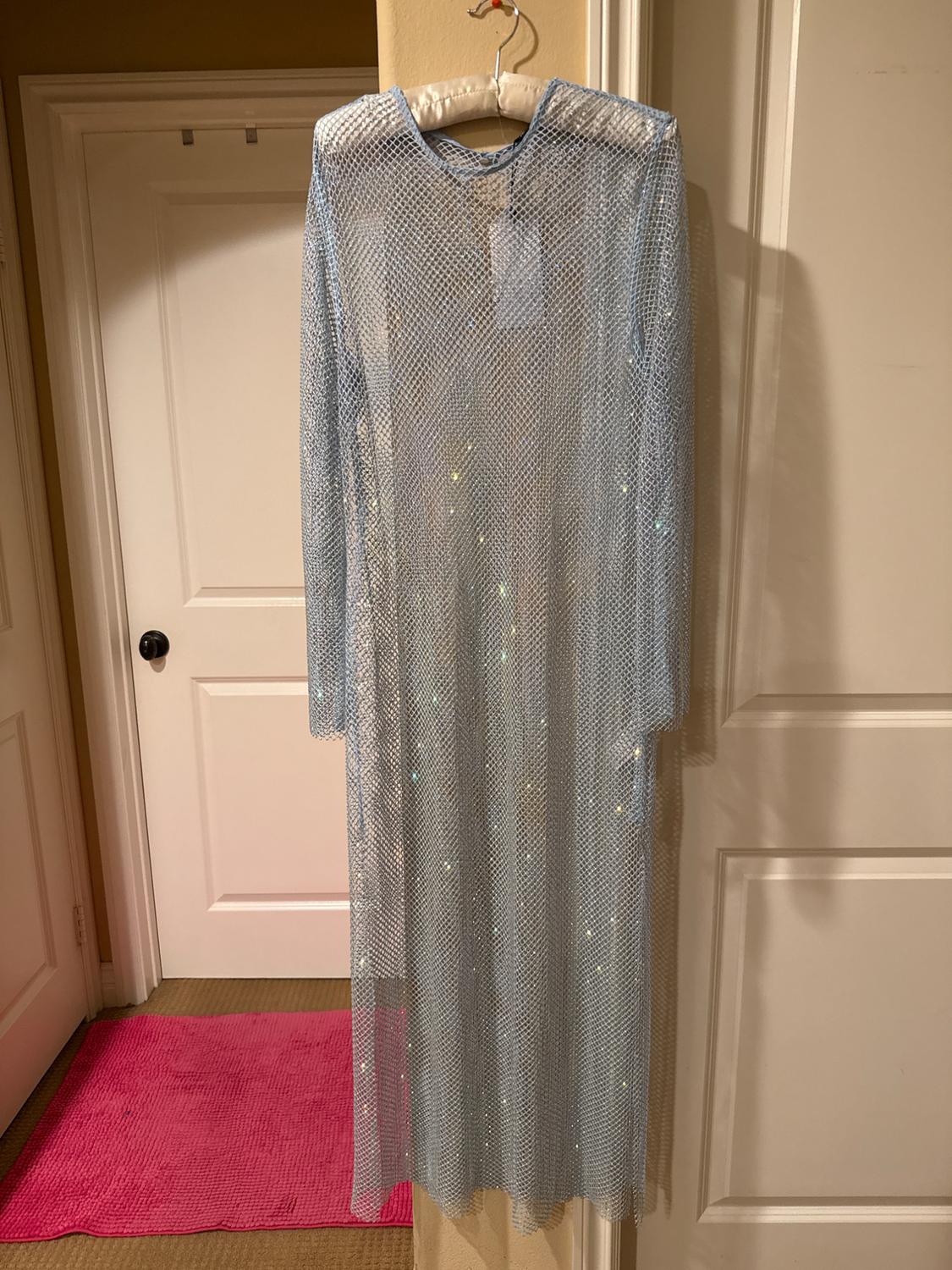 Shiny blue mesh maxi dress hanging on a hanger, over a white door. Pink rug on the floor.