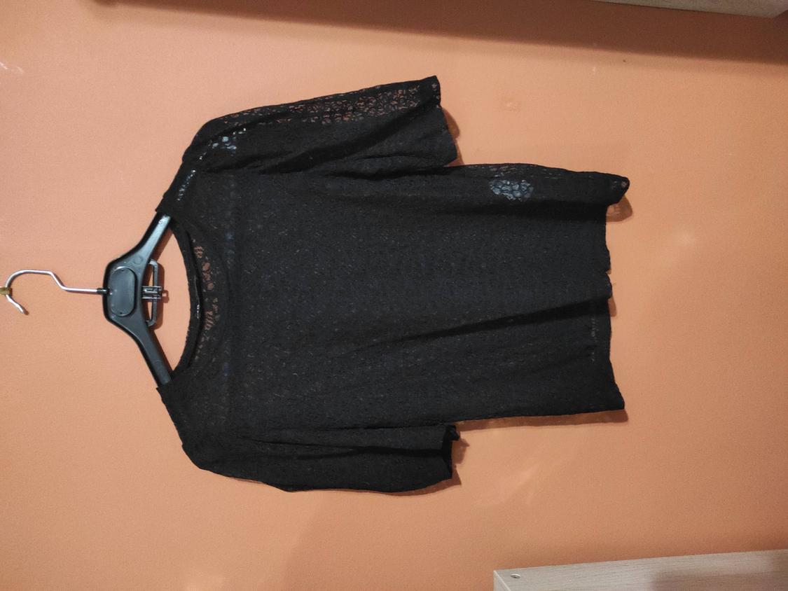 Black lace blouse hanging on a hanger against an orange wall.