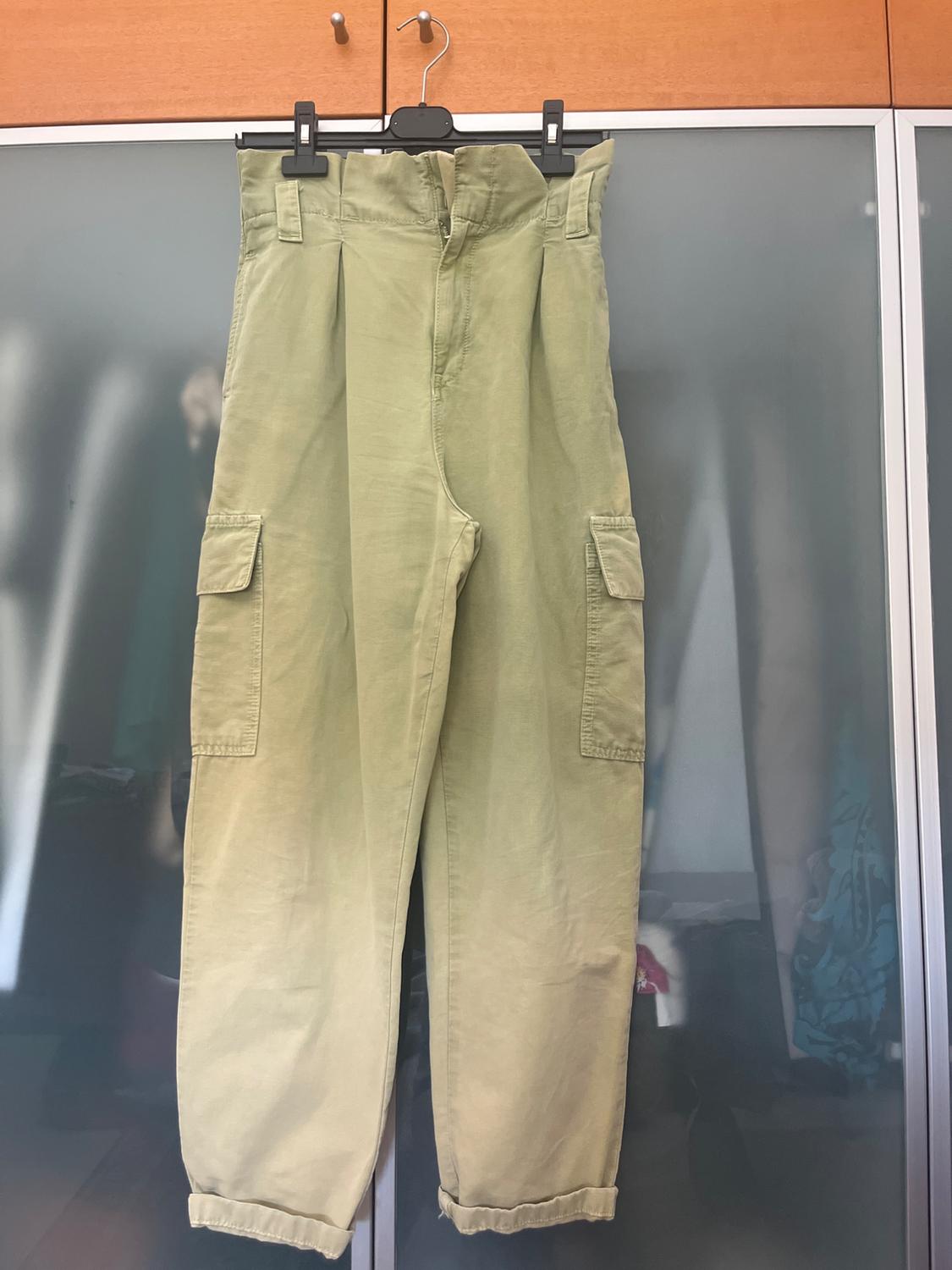 Light green cargo trousers with a ruched waist and side pockets, hanging on a hanger in front of a wardrobe.