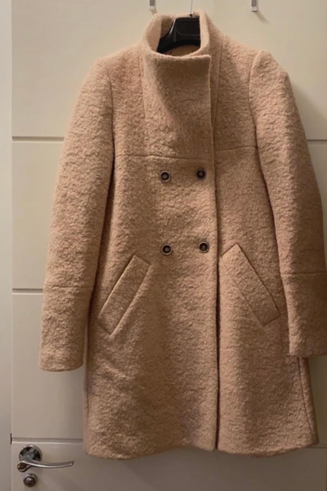 Front view of a beige coat with a high neck and side pockets.