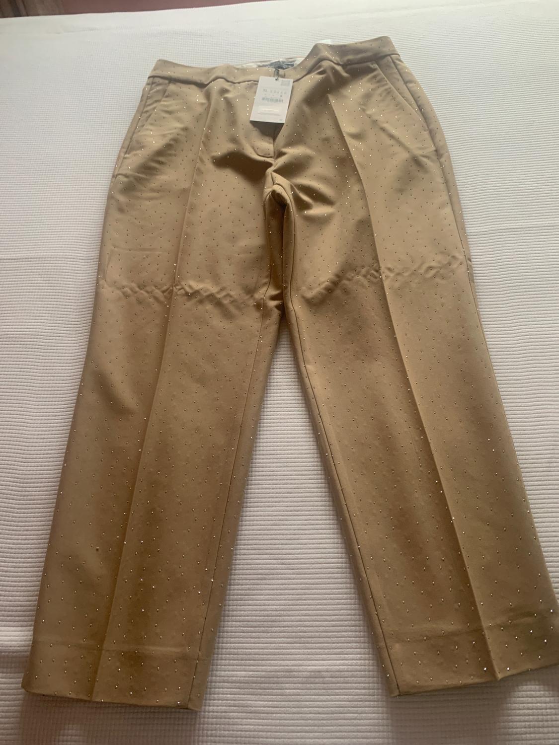 Beige trousers with small glittery dots, visible hang tag, on a textured white surface.