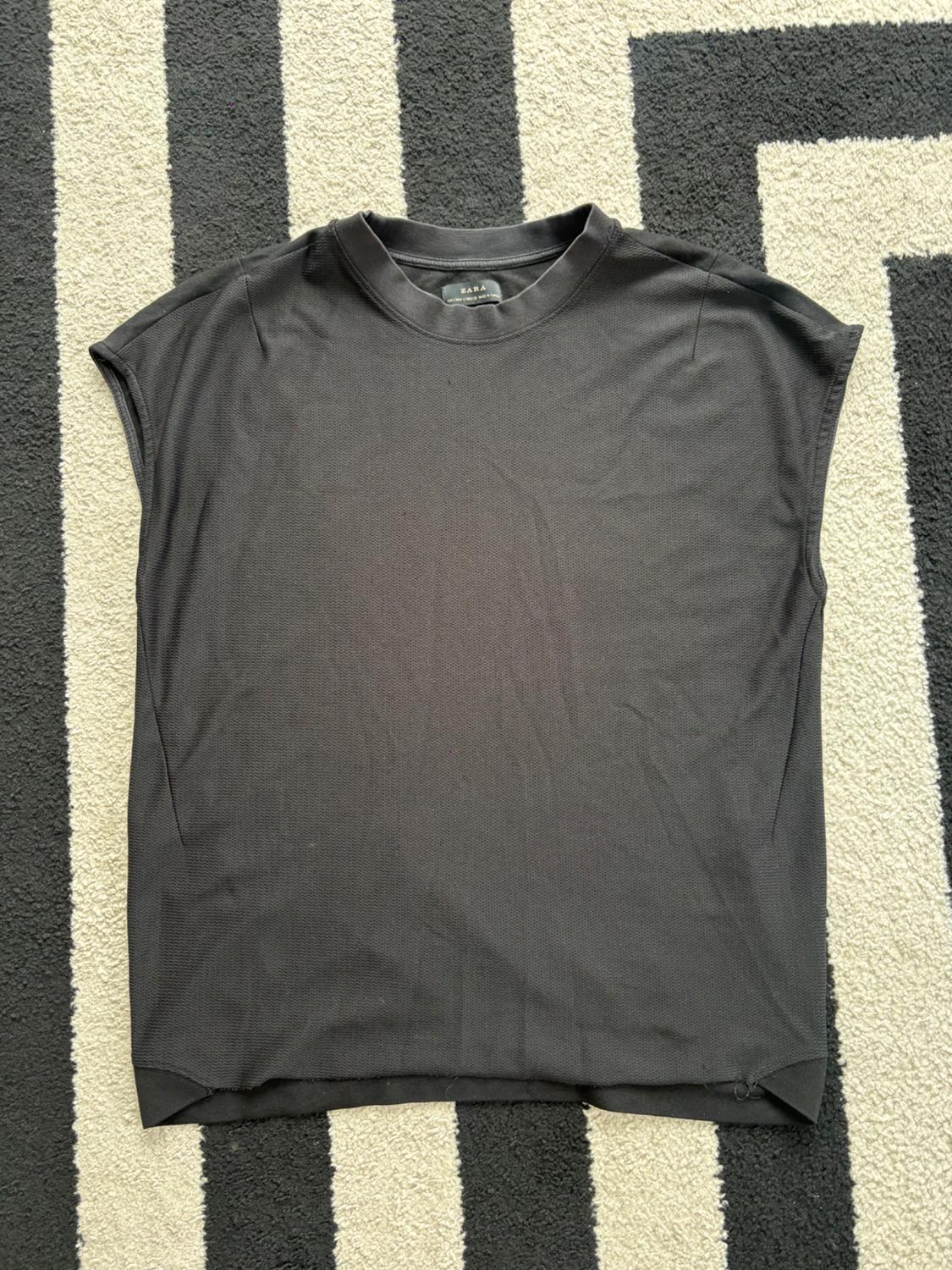 Black sleeveless t-shirt on a black and white striped rug. Visible tag on the collar.
