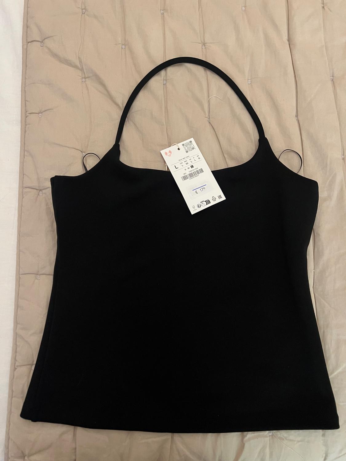 Black camisole top with a label showing size L and €17.95, laid out on a beige quilted blanket in a relaxed style.