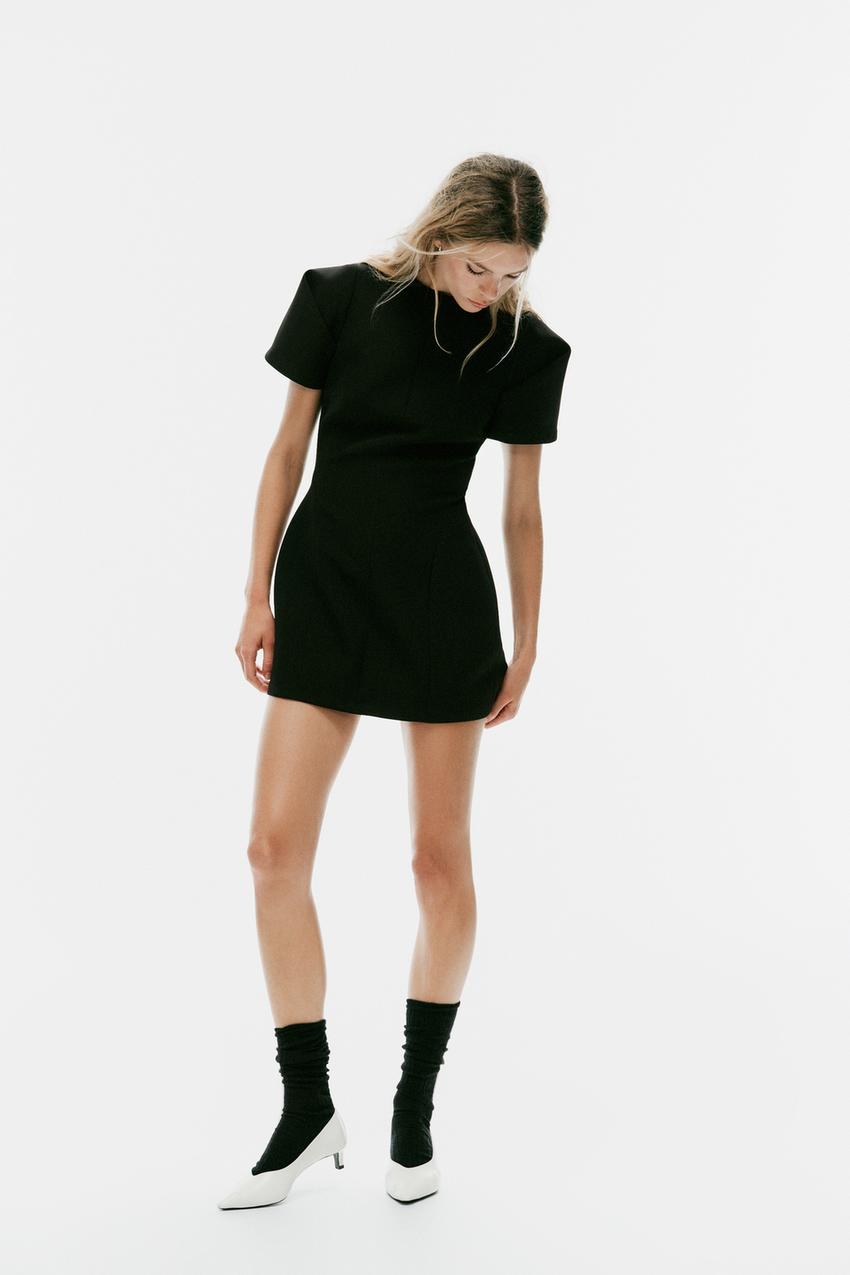 Black crew neck mini dress set with short pleated sleeves and exposed seams, black socks and white shoes.